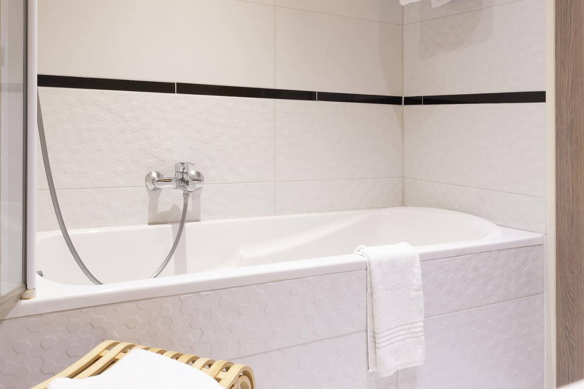 A modern bathroom with a bathtub, a shower, and a wooden stool.