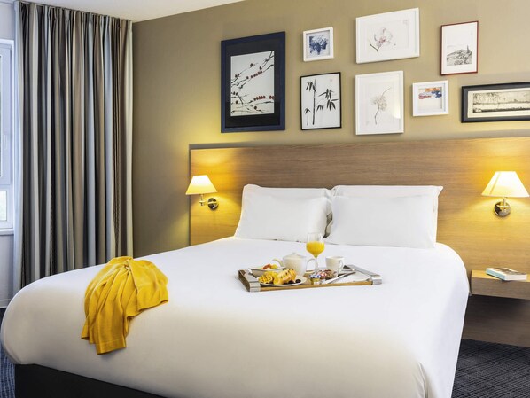 A hotel room with a large bed, two bedside lamps, a tray of breakfast, and wall art.