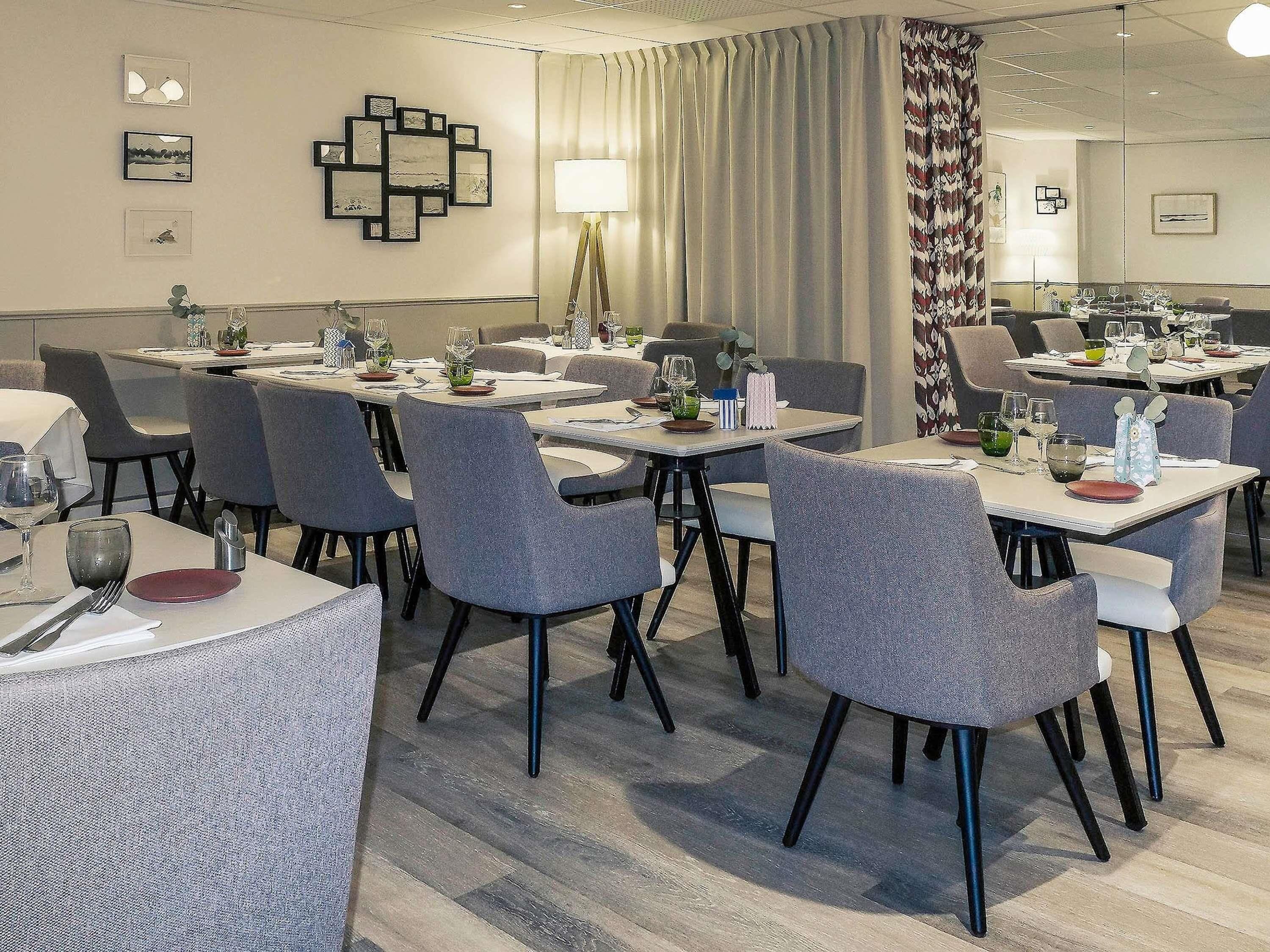 A dining area with tables set for meals, grey upholstered chairs, and a wall with framed artwork.