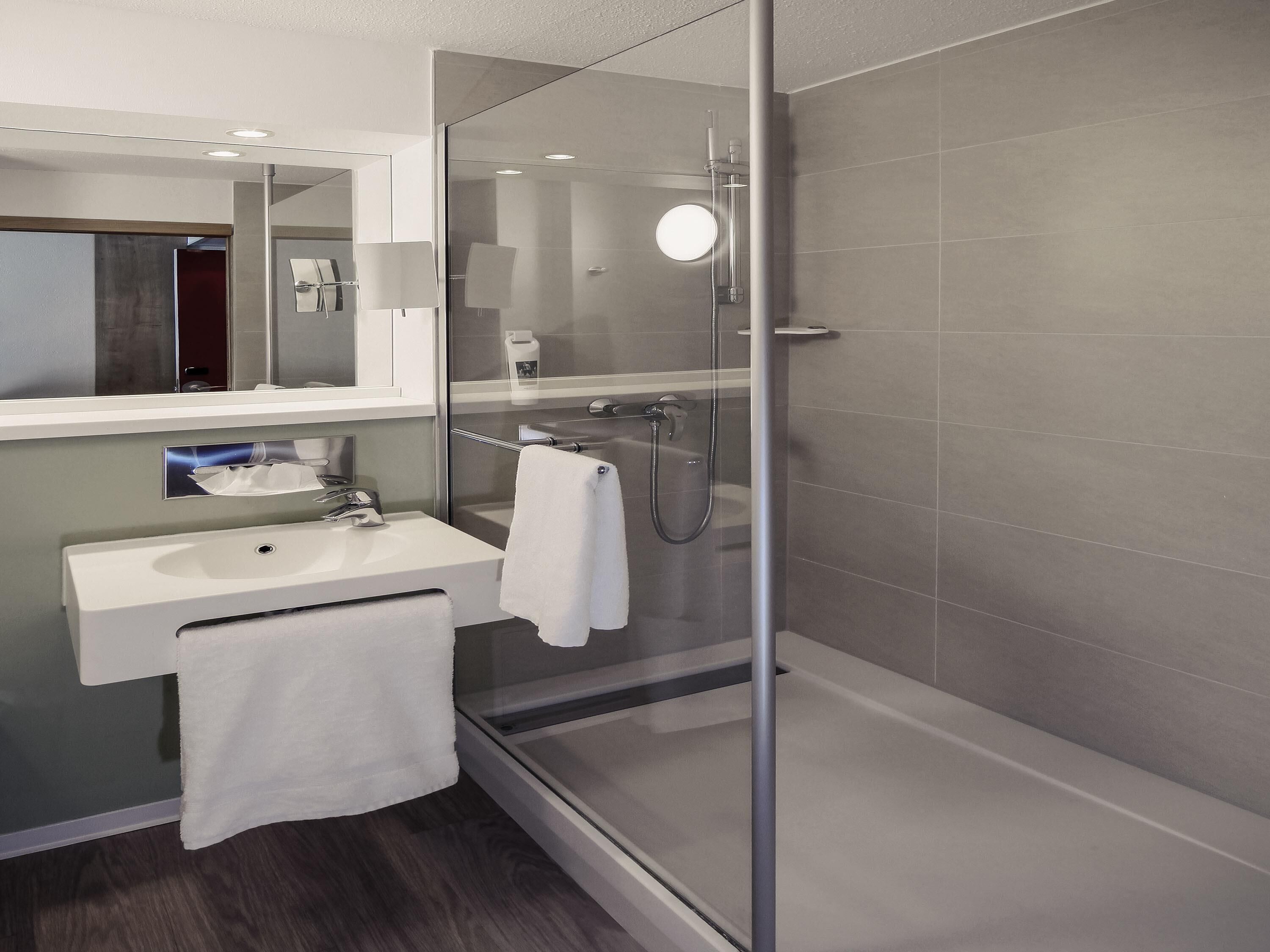 A modern bathroom with a glass shower enclosure, a sink with a towel, and a mirror.
