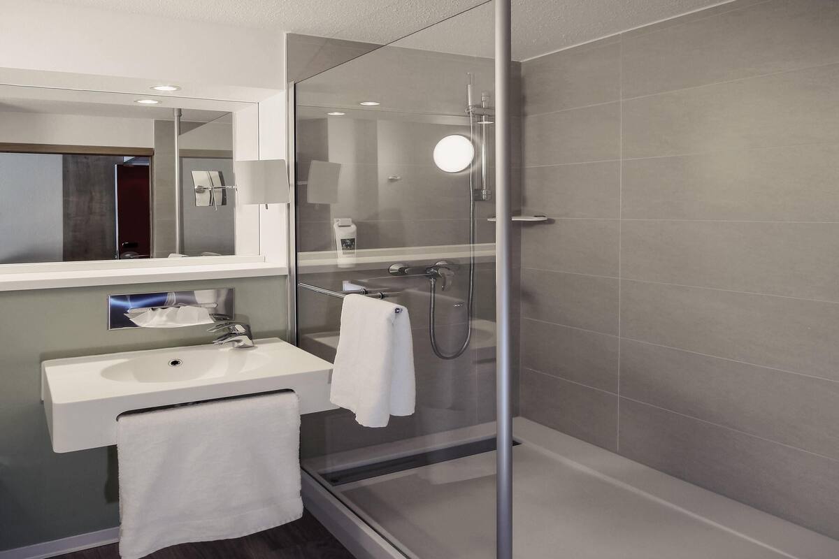 A modern bathroom with a glass shower enclosure, a sink with a towel, and a mirror.