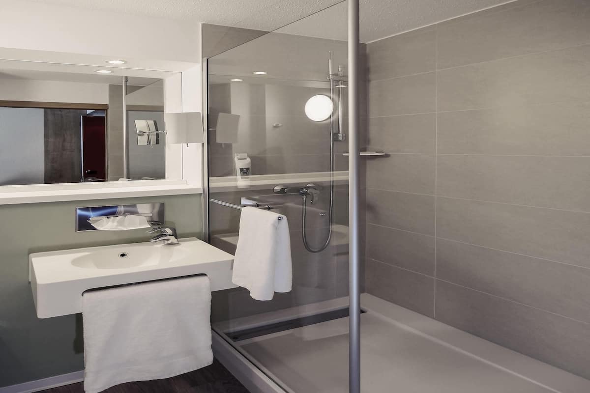 A modern bathroom with a glass shower enclosure, a sink with a towel, and a mirror.