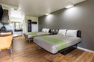 Una habitación de hotel compacta con dos camas, un kitchenette y una zona de estar.