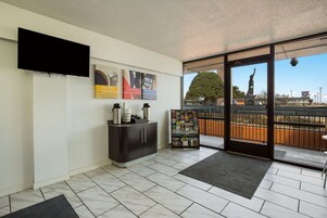 Un moderno vestíbulo de hotel con una televisión de pantalla plana, una estación de café, un atril para revistas y vistas a una estatua a través de amplias puertas de cristal.