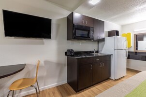 Una cocina compacta con armarios oscuros, microondas, tostadora y refrigerador.