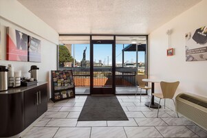 Vestíbulo de hotel con recepción, estación de café, estante de revistas y vistas al exterior.