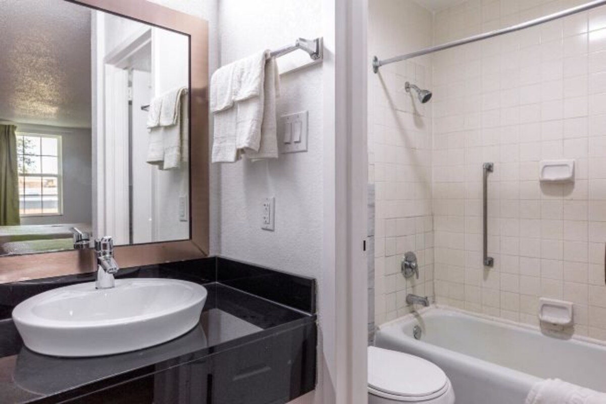 A bathroom with a white sink, black countertop, and a bathtub.