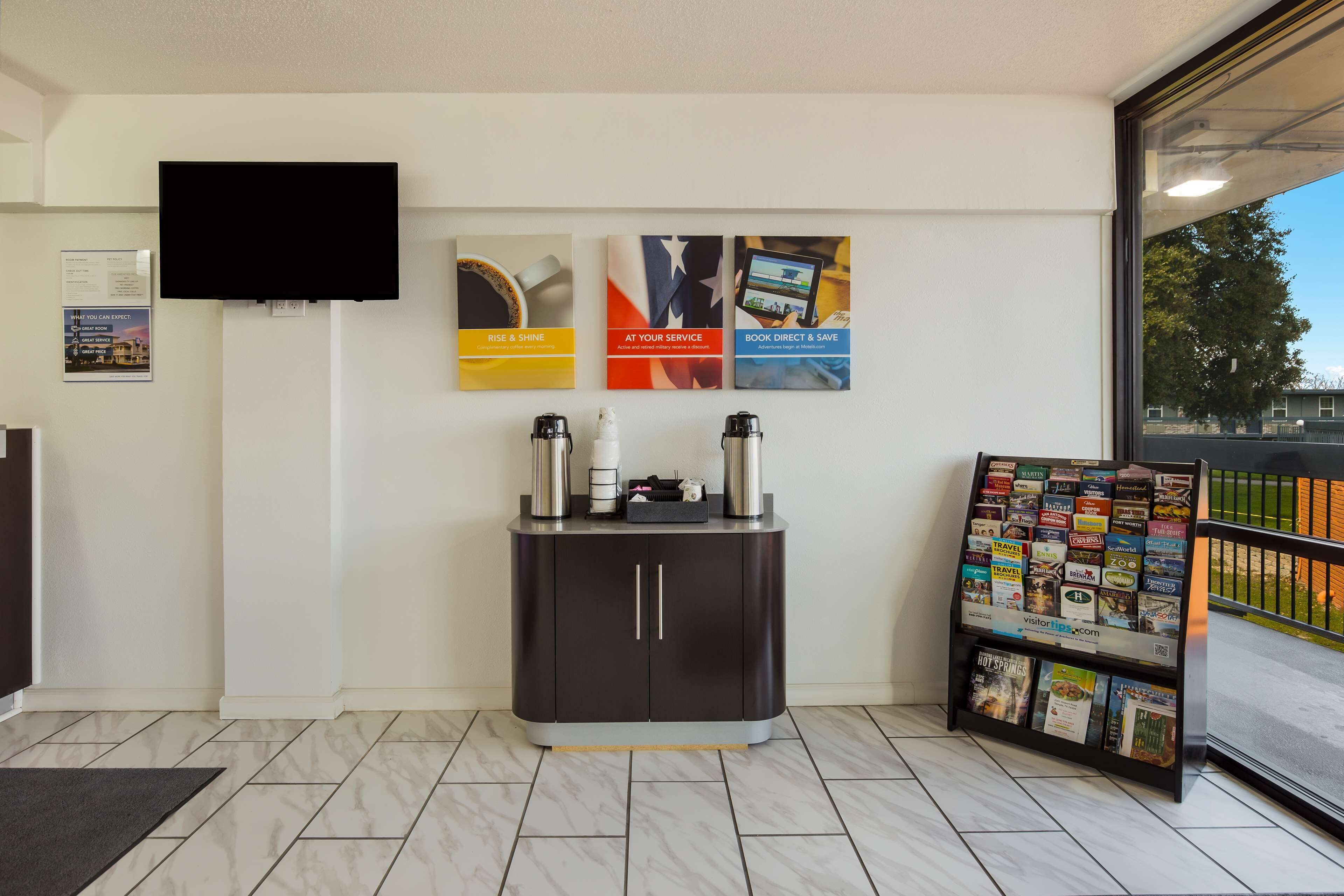 A reception area with a dark-colored desk, a flat-screen TV mounted on the wall, and a bulletin board with travel brochures.