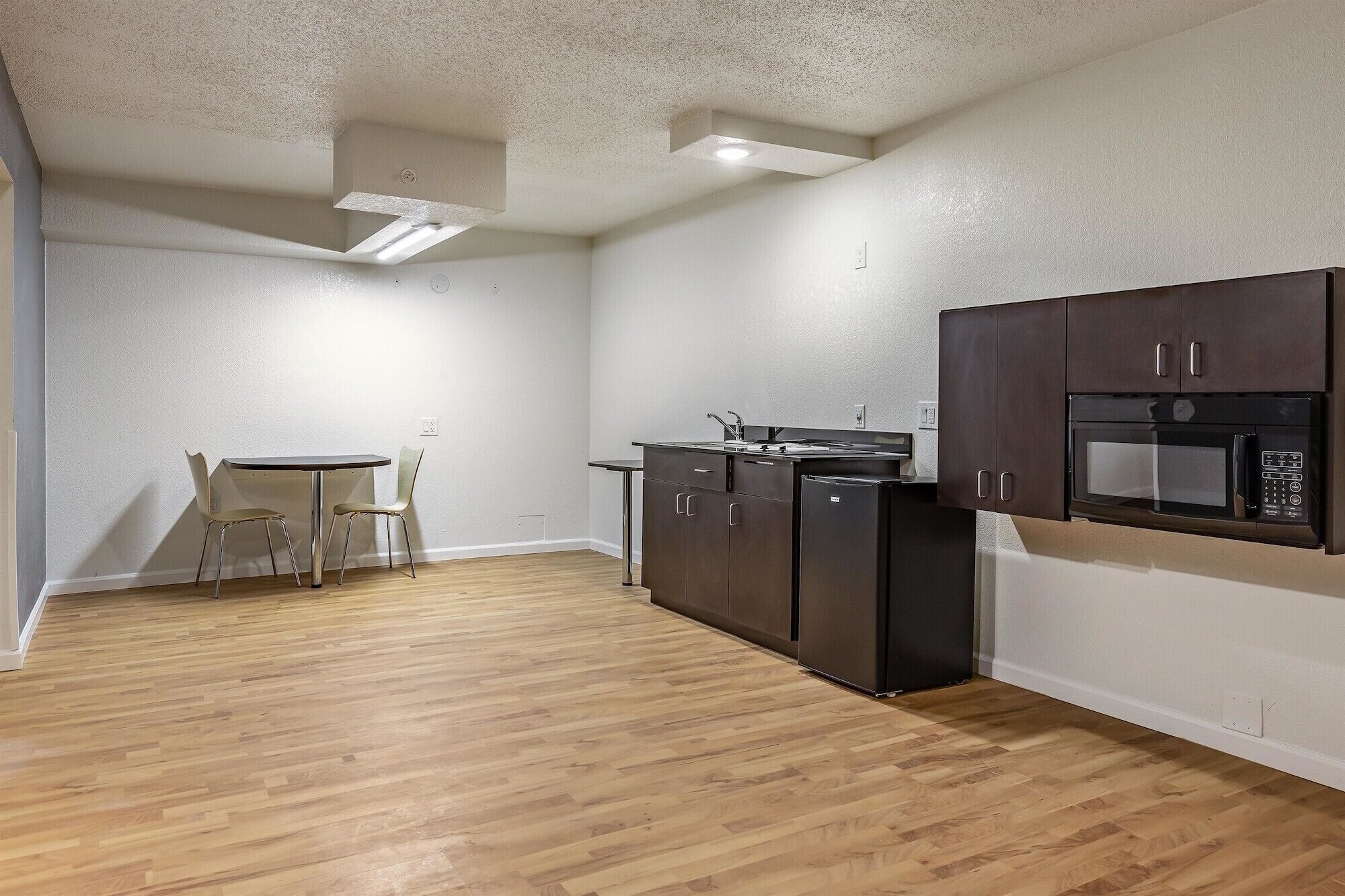A compact kitchen with a dishwasher, microwave, and dark cabinets. There is a small table with two chairs in the corner.