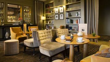 A well-lit lounge area with comfortable seating, a bar with glassware, and a bookshelf with books.