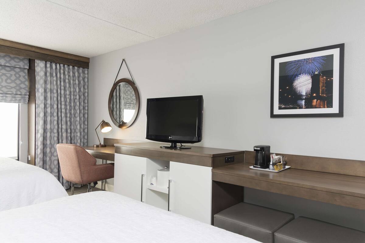 A hotel room with a bed, a desk with a television, a chair, a coffee maker, and a framed picture on the wall.