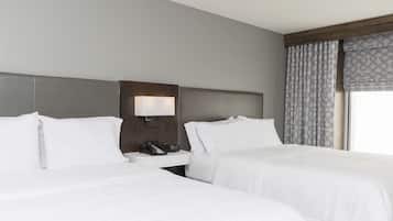 A hotel room with two beds, a nightstand with a lamp, and a window with patterned curtains.