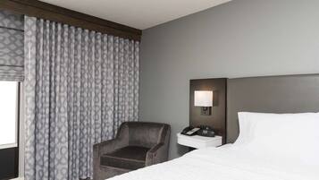A hotel room with a bed, a chair, a nightstand with a phone, and a wall-mounted lamp.