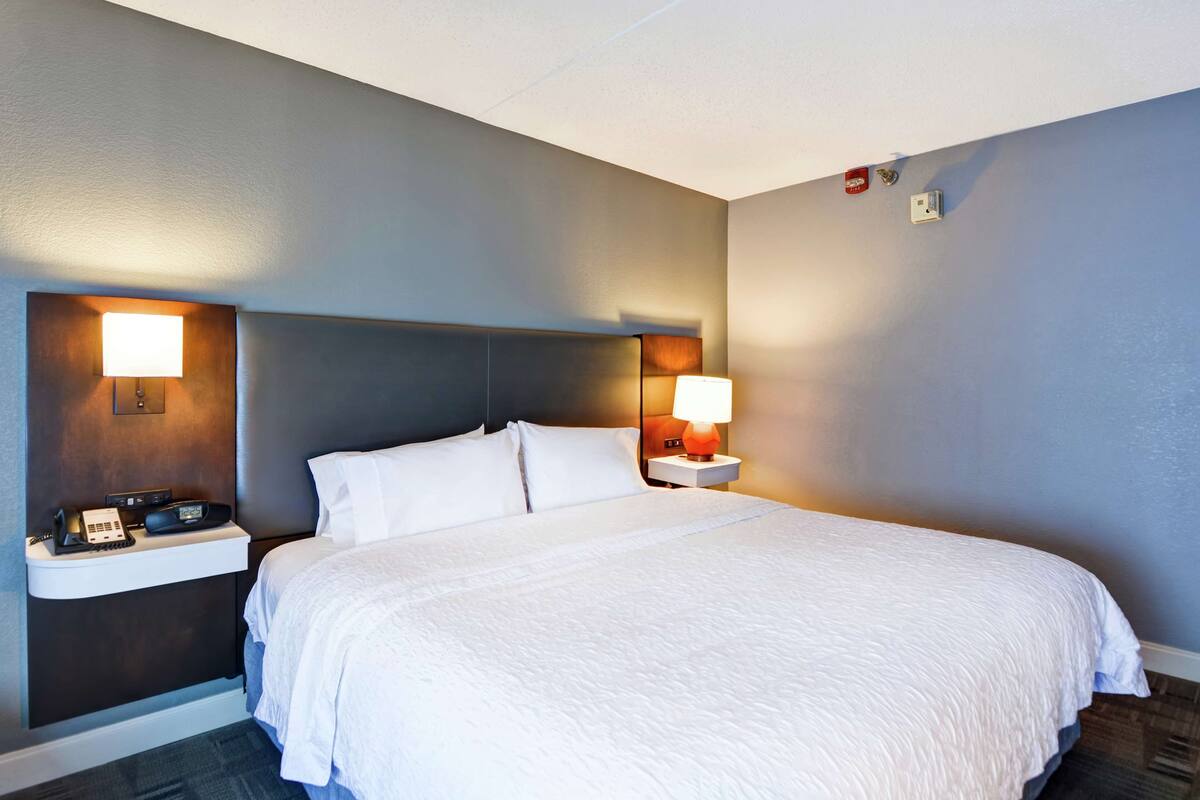 A hotel room with a large bed, two bedside tables, a nightstand, and wall-mounted lamps.