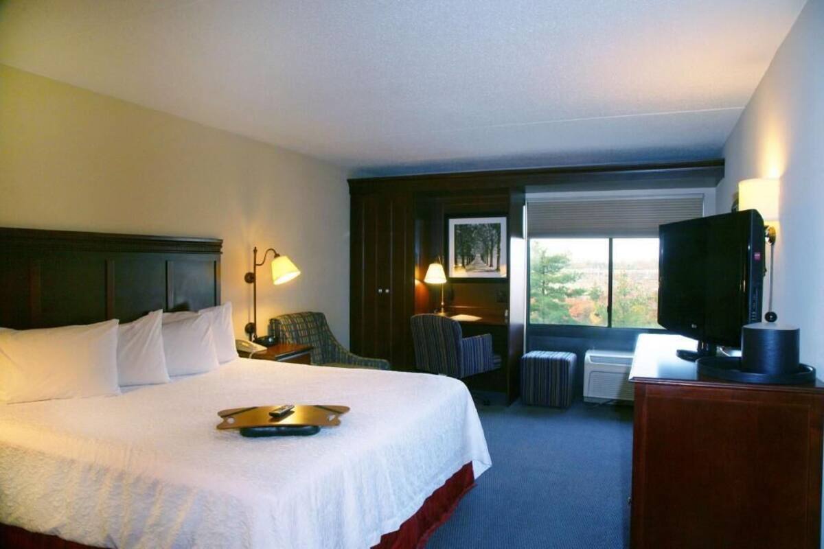 A hotel room with a bed, bedside lamps, a television, a desk, and a window with a view.