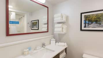A hotel bathroom with a large mirror, white sink, and shelves with towels.