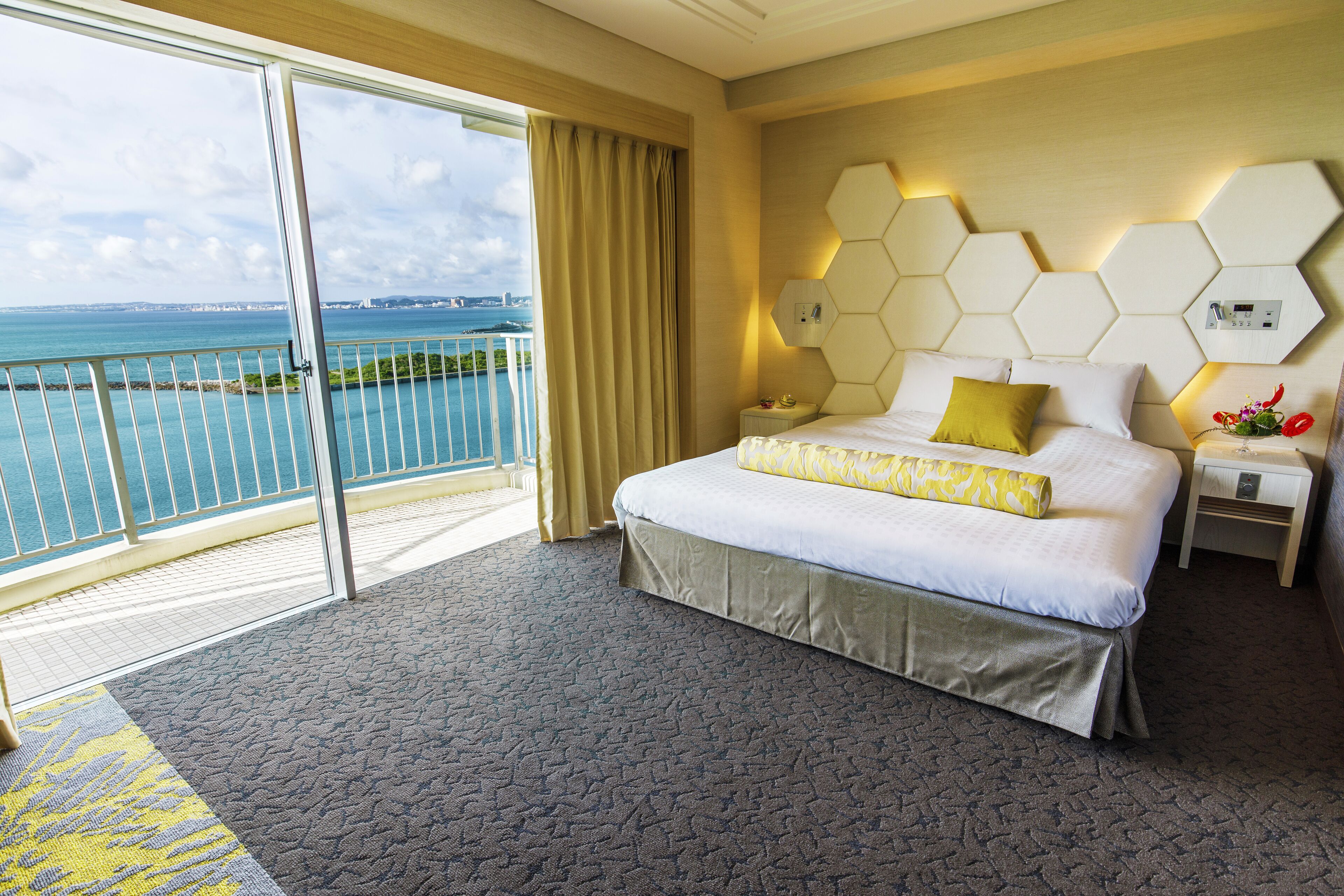 Habitación de hotel con una cama grande, una mesita de noche, vista al mar y un balcón.