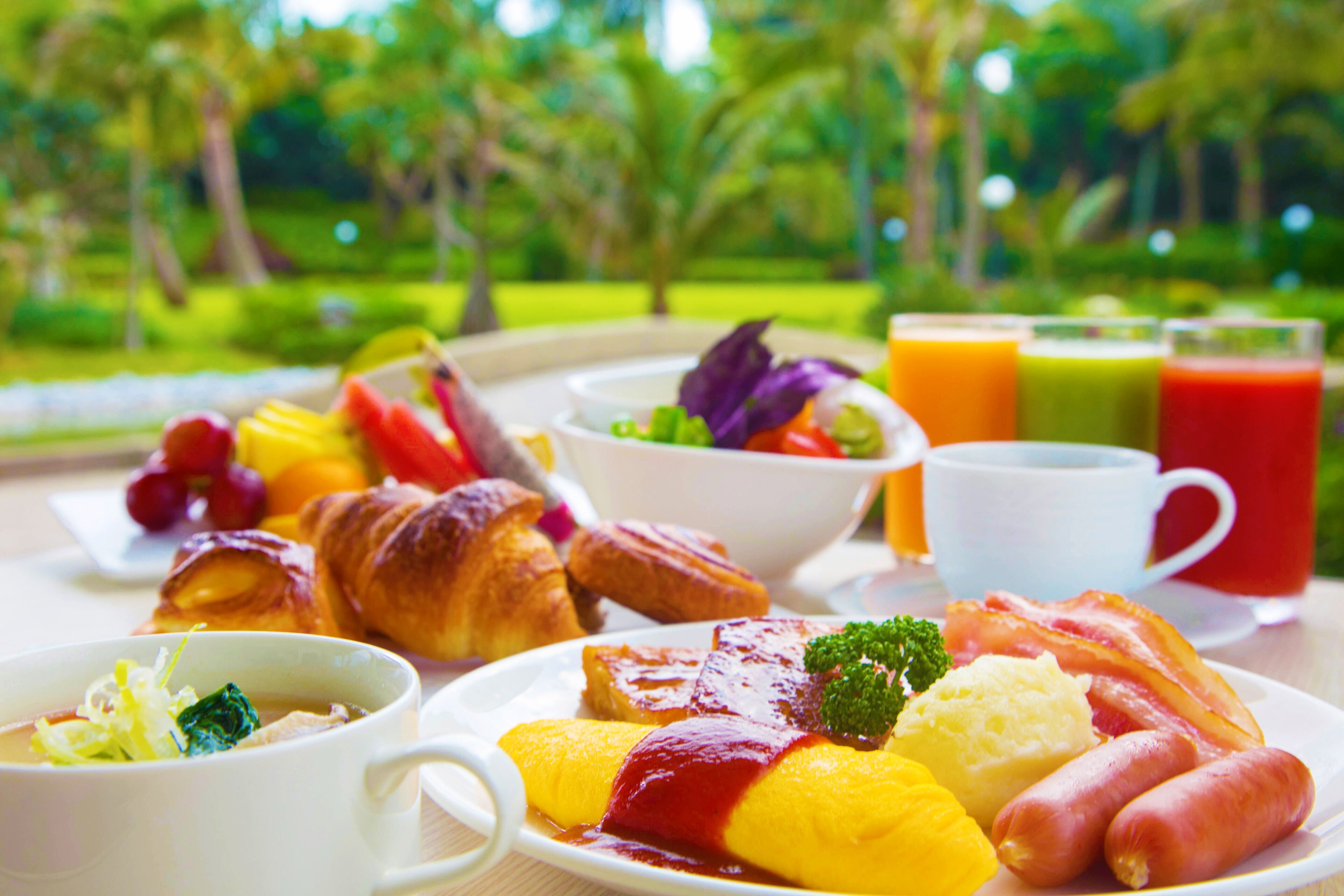 Ein Frühstückstisch mit Croissants, Eiern, Würstchen und verschiedenen Früchten und Gemüsesorten.