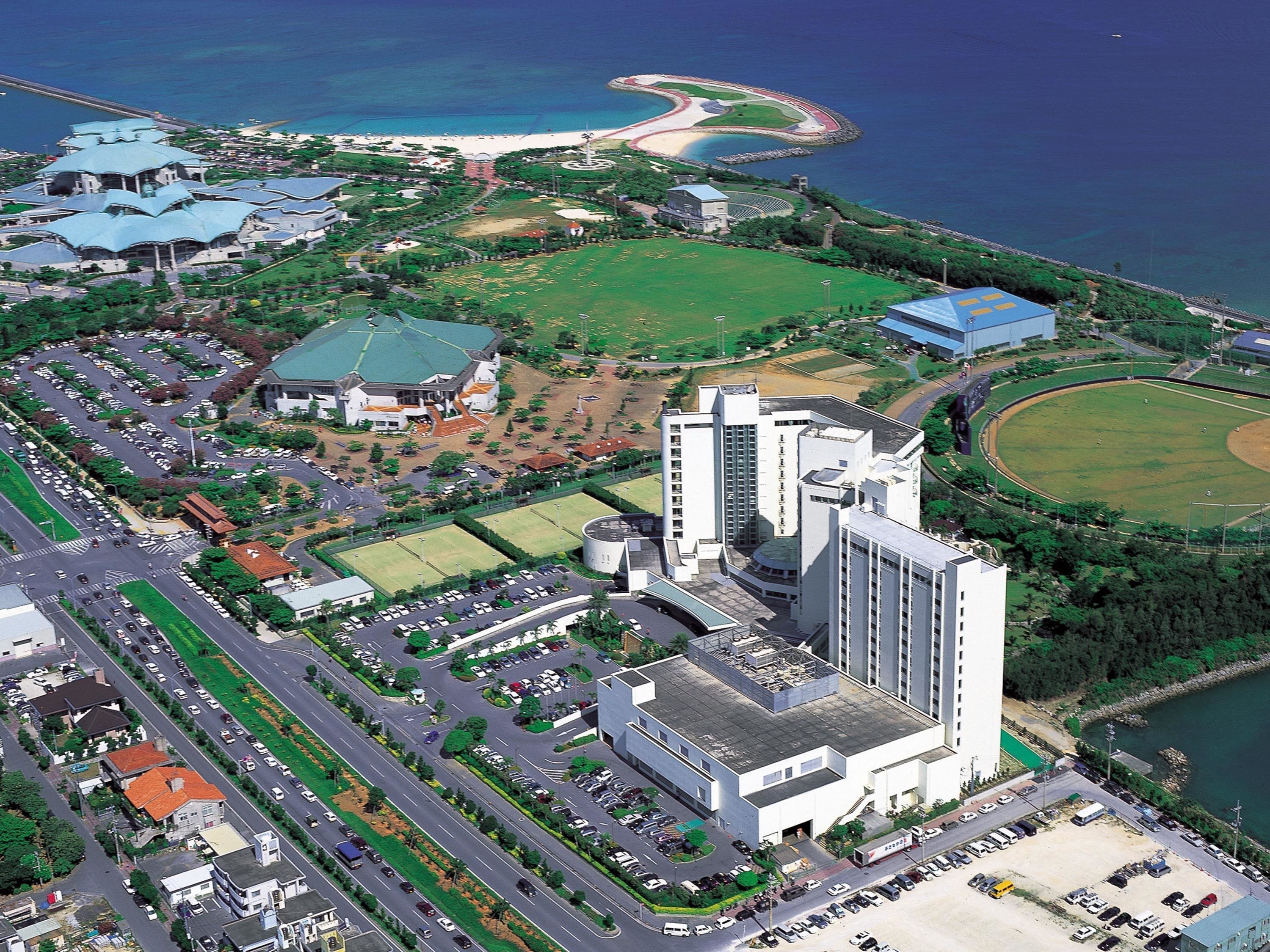An aerial view of a coastal urban area with a large building complex, roads, and a beach.