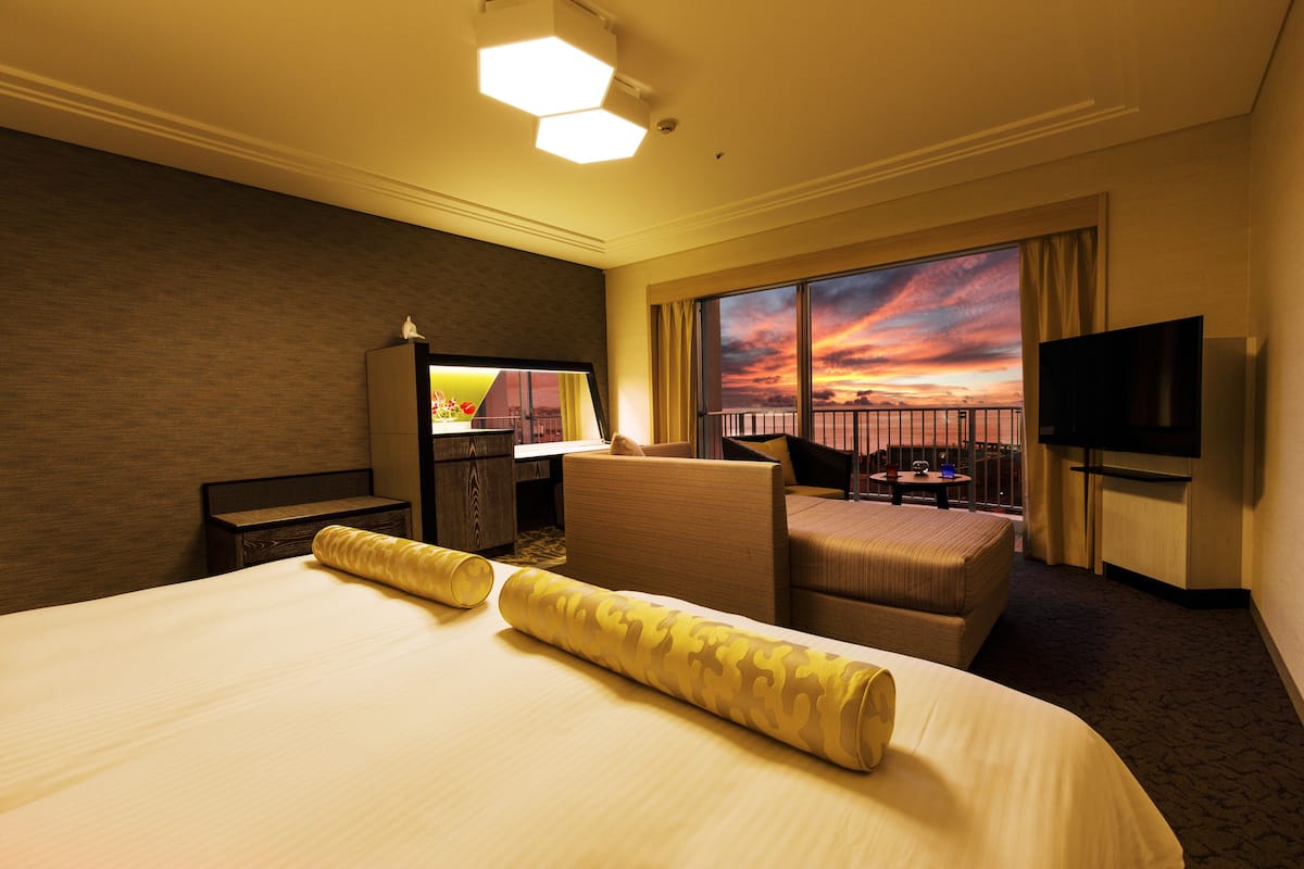 Une chambre d’hôtel avec un grand lit, un coin salon offrant une vue sur le coucher du soleil et une télévision.