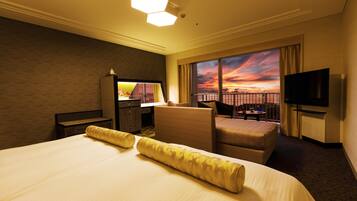 A hotel room with a large bed, a seating area with a view of the sunset, and a television.