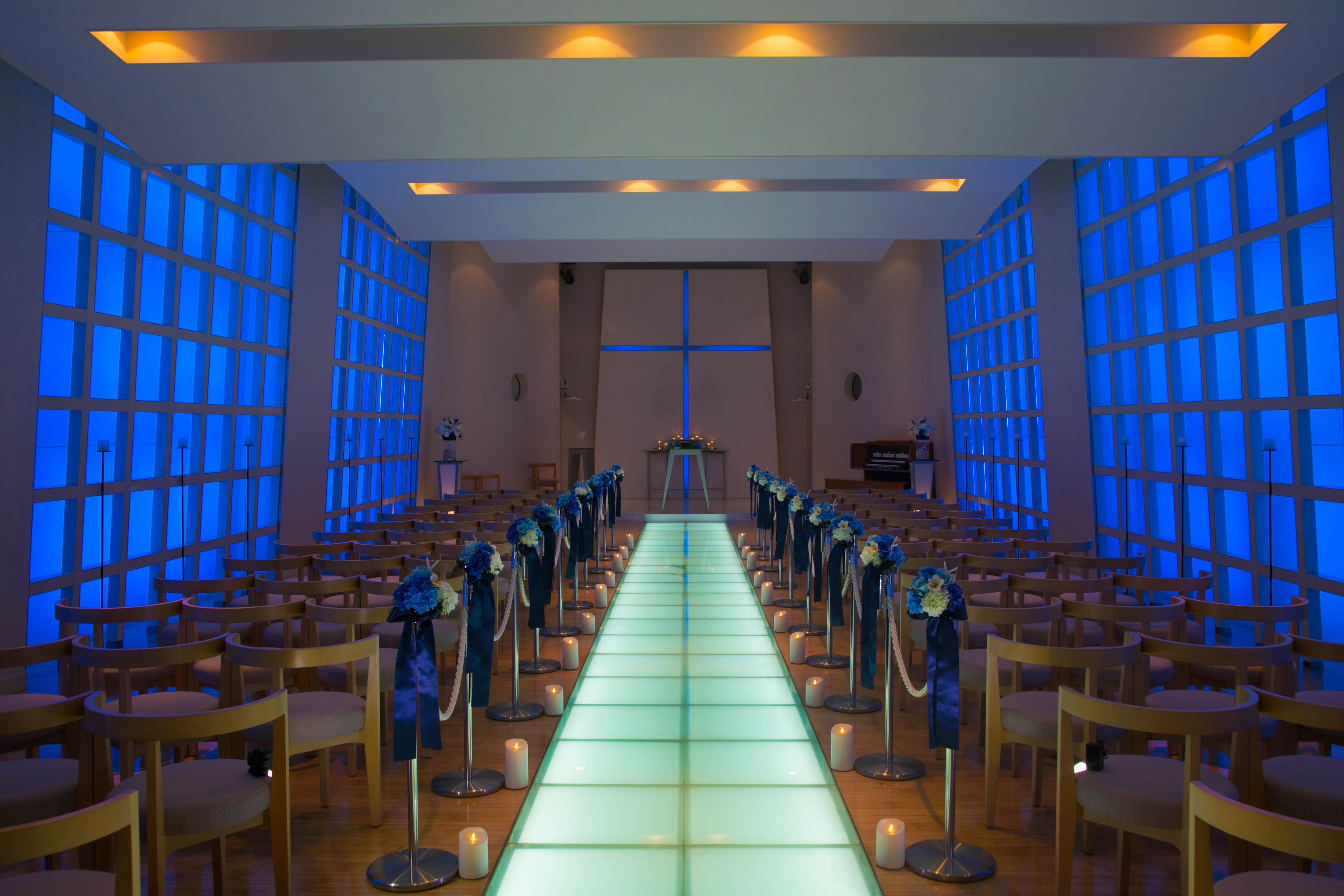 A church interior with rows of wooden pews, a central aisle, and a cross at the front.