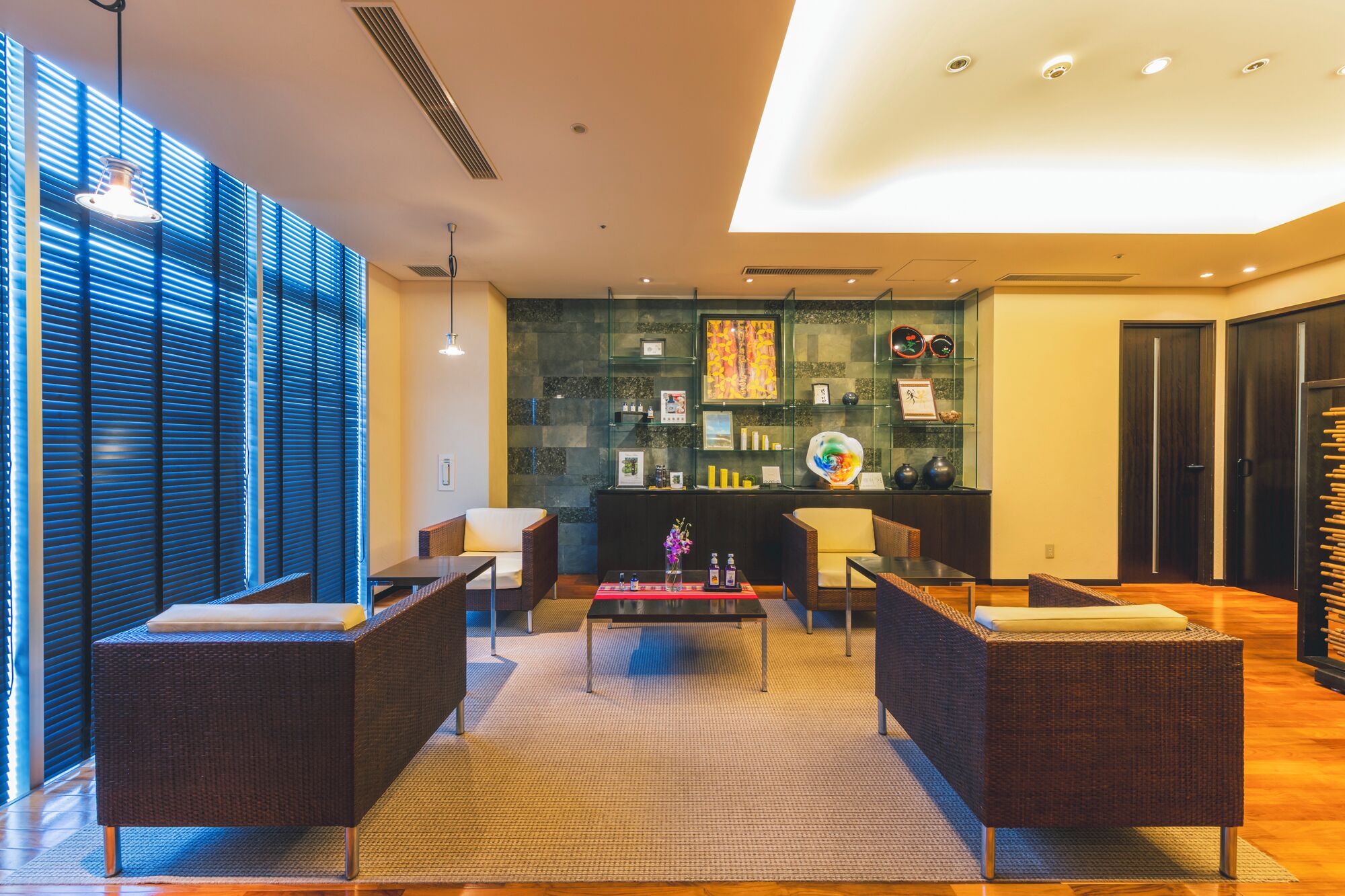 A modern lobby with wicker furniture, a central coffee table, and a glass display case with various items.