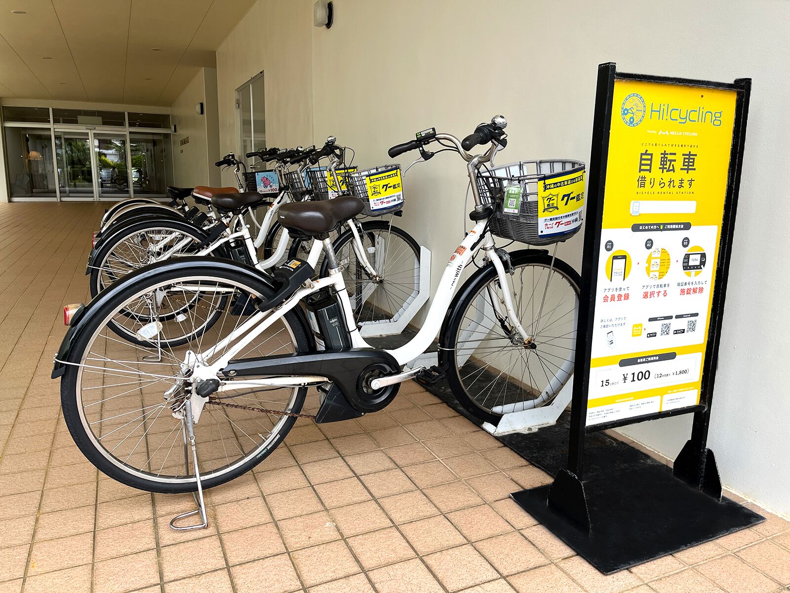 Una estación de alquiler de bicicletas con varias bicicletas estacionadas y un cartel con información sobre los precios.