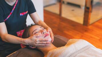 A person receiving a facial treatment in a room with wooden flooring and a visible chair.