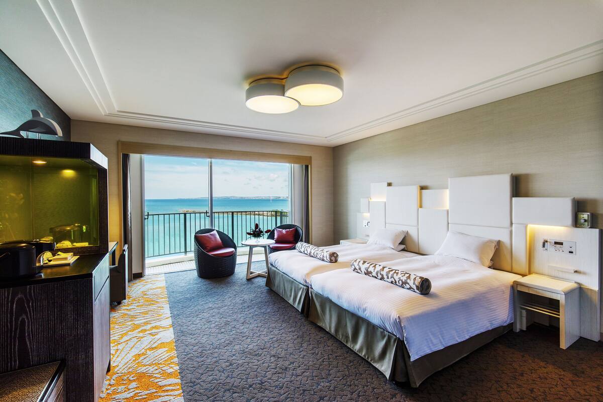 Une chambre d’hôtel avec un grand lit, un bureau, une chaise, une petite table et une vue sur la mer.