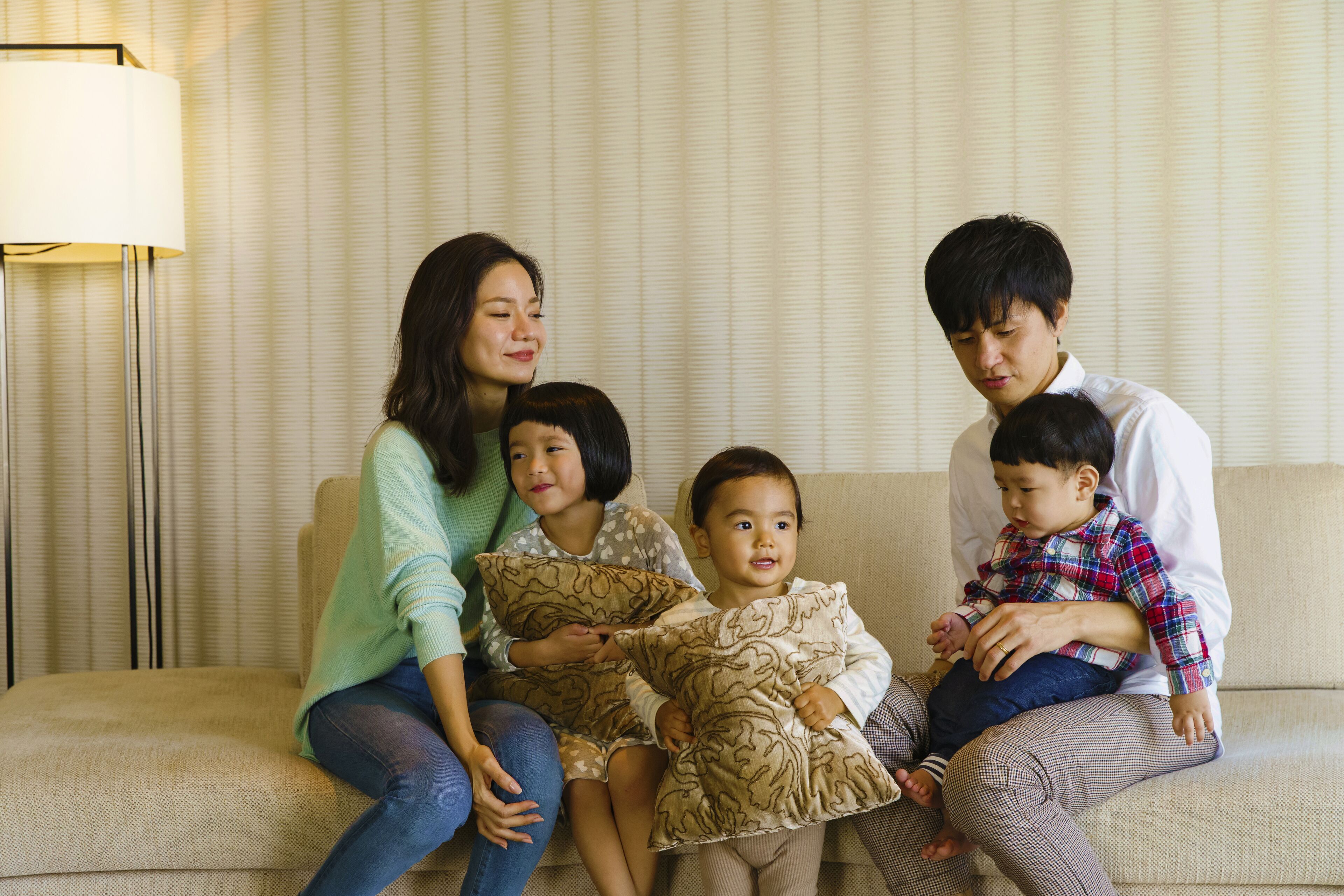 Une famille est assise sur un canapé beige, avec une lampe en arrière-plan.