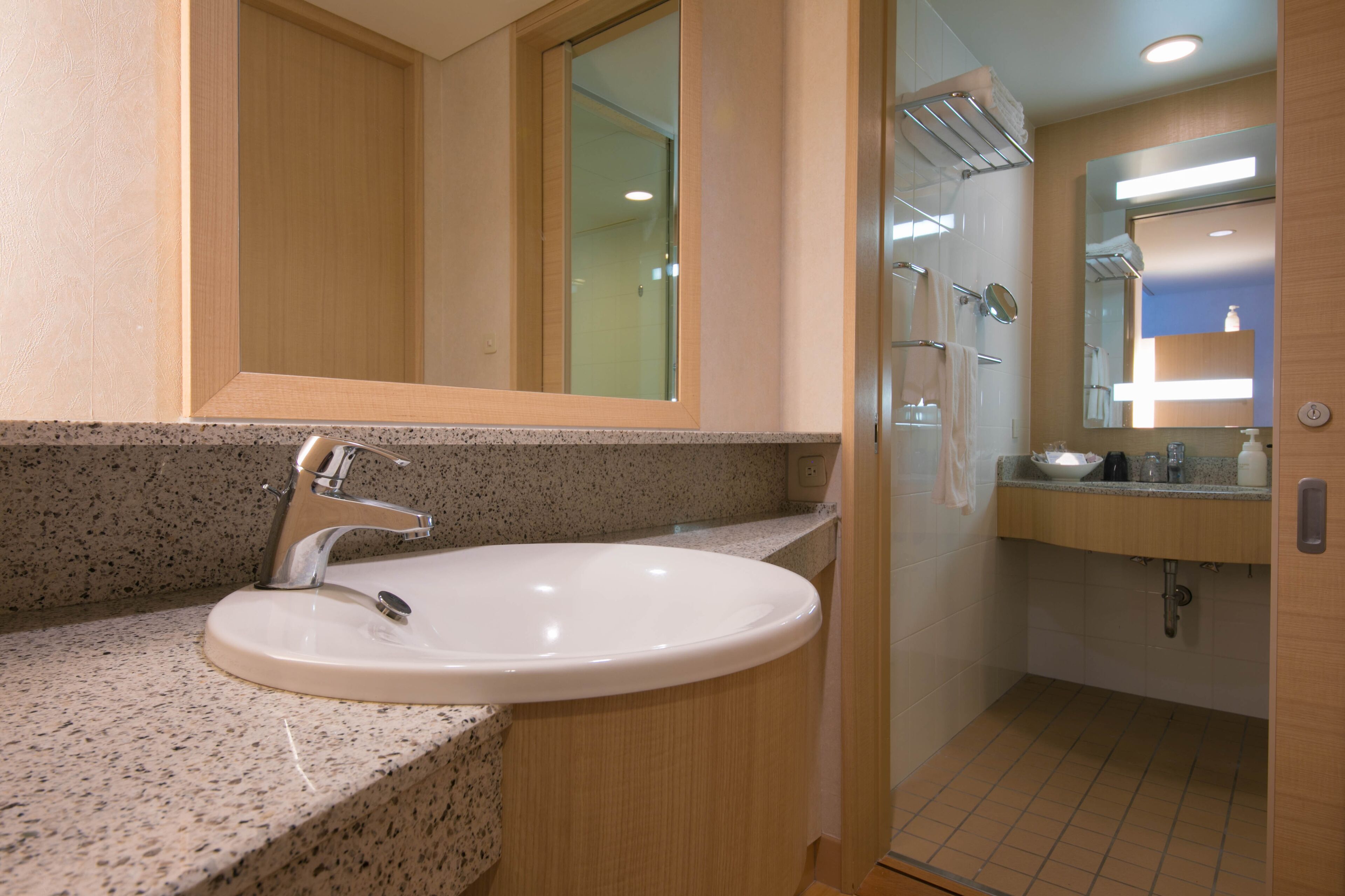 Un baño con encimera de granito, un lavabo blanco, un espejo y zona de ducha.