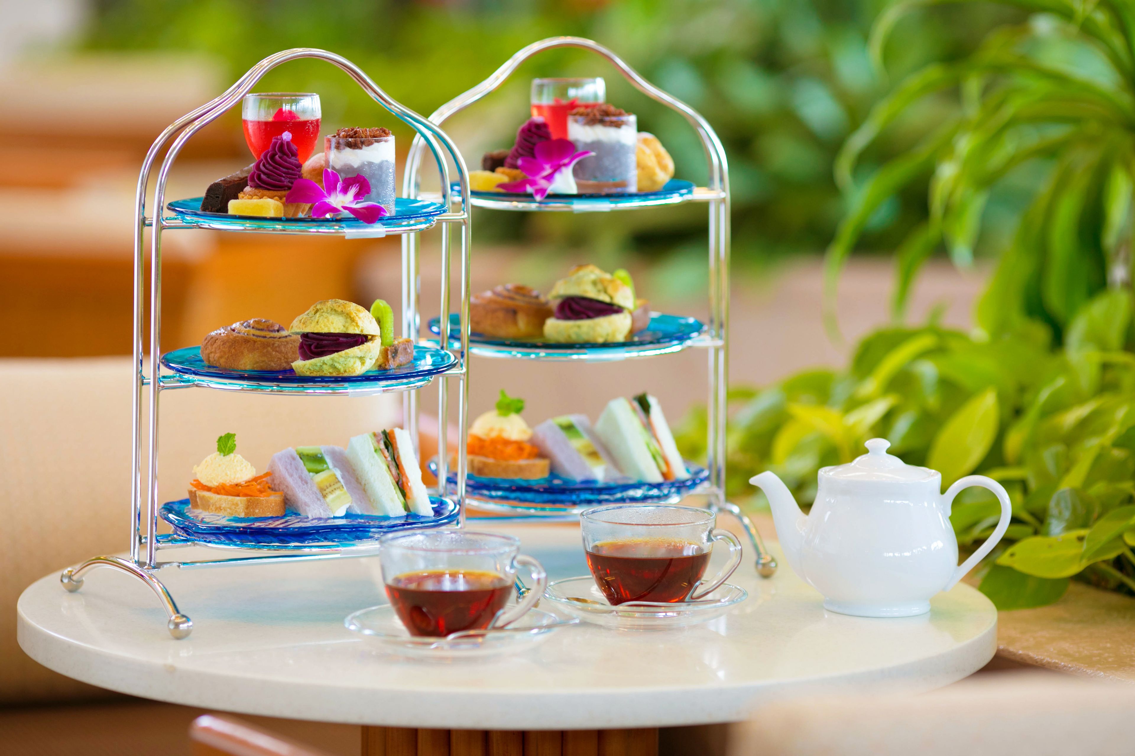 A three-tiered dessert stand with various pastries and a teapot on a round table.