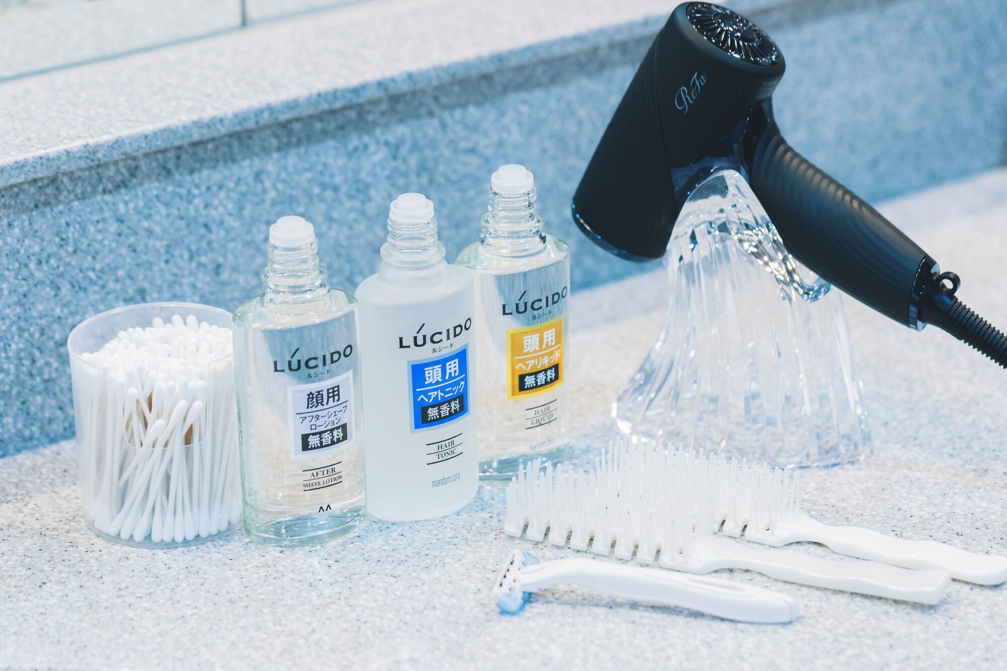 A hair care setup with a hairdryer, cotton swabs, and bottles of Lúcido hair products on a countertop.