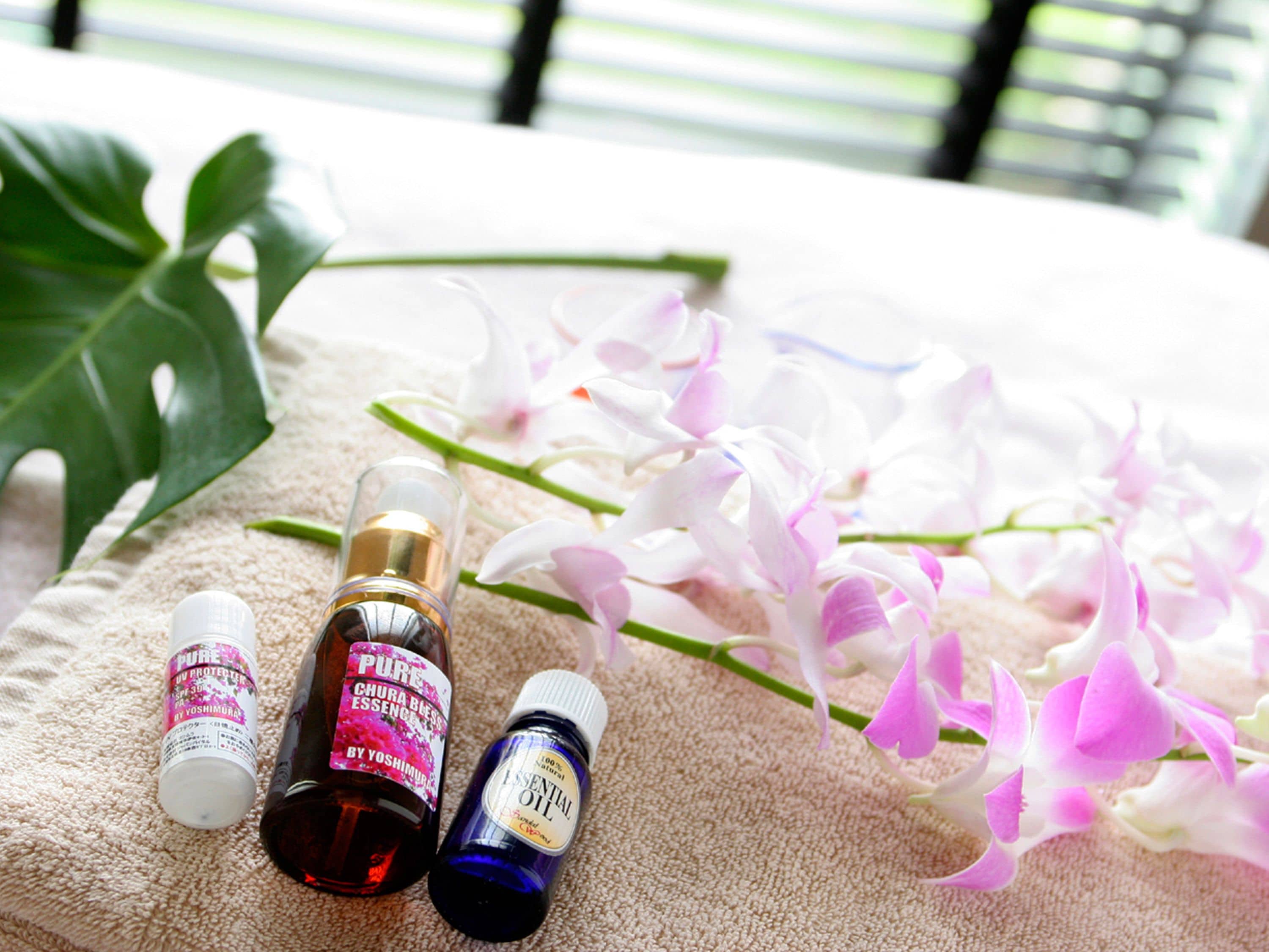 Bottles of essential oil and flowers on a beige towel.