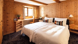 Une chambre à coucher aux murs lambrissés, avec un grand lit, une table de chevet, une fenêtre avec des rideaux et une chaise en bois.