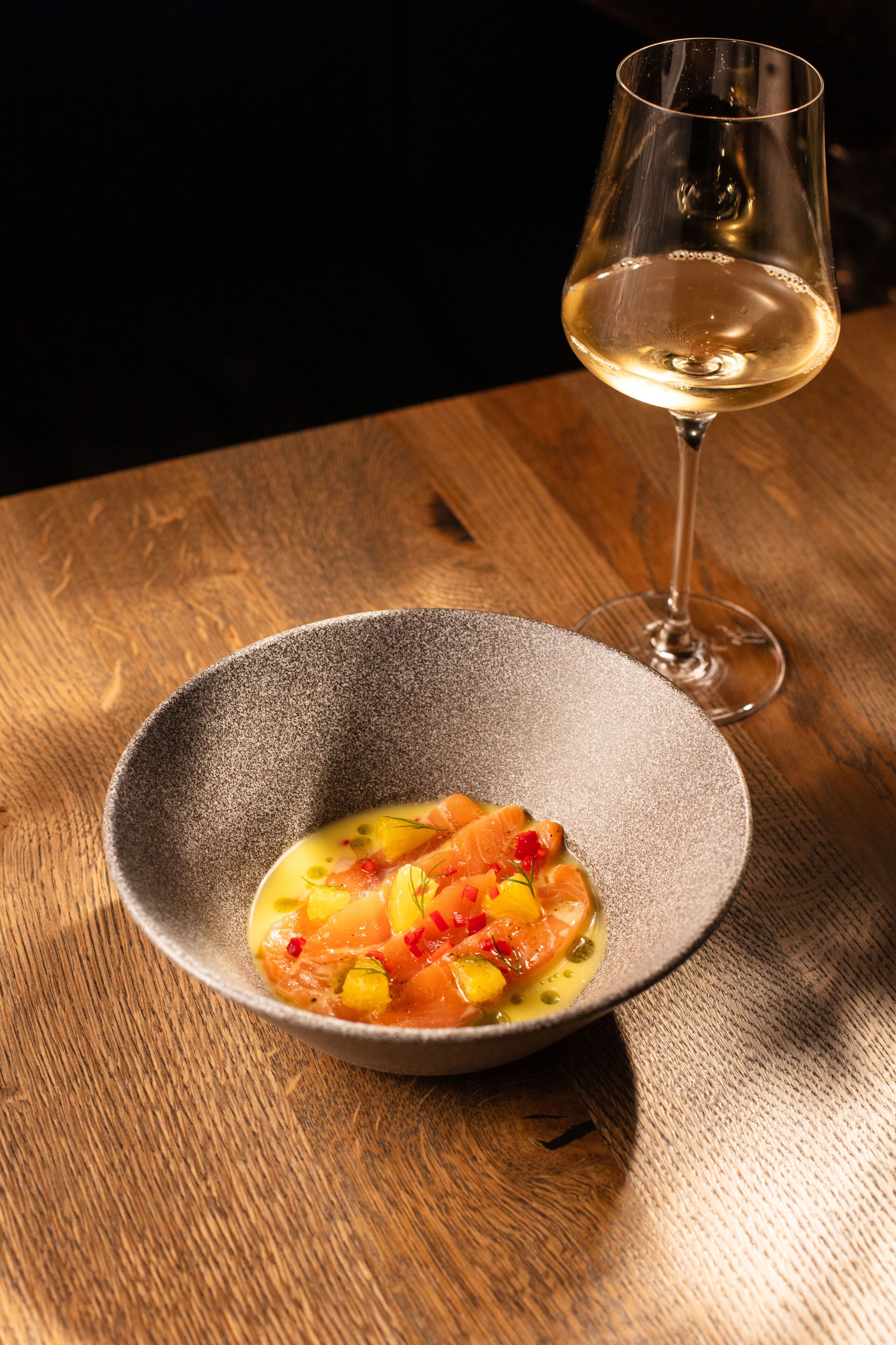 Un plato de comida con una copa de vino blanco sobre una mesa de madera.