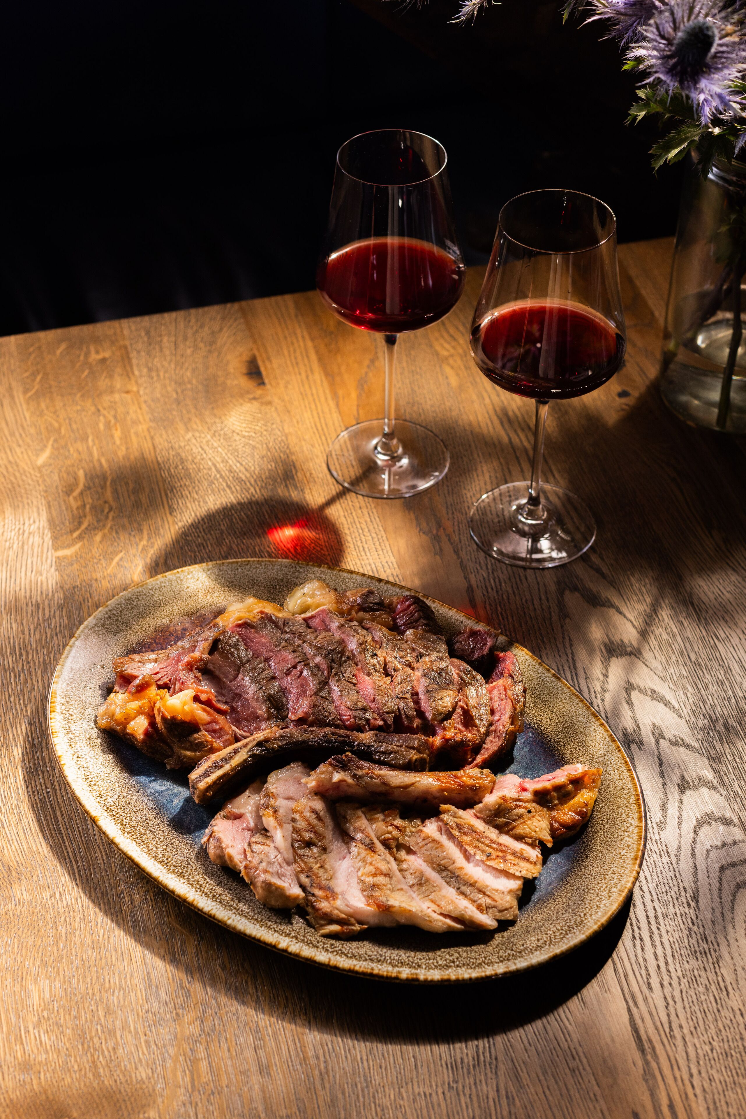 A plate of sliced meat and two glasses of red wine on a wooden table.