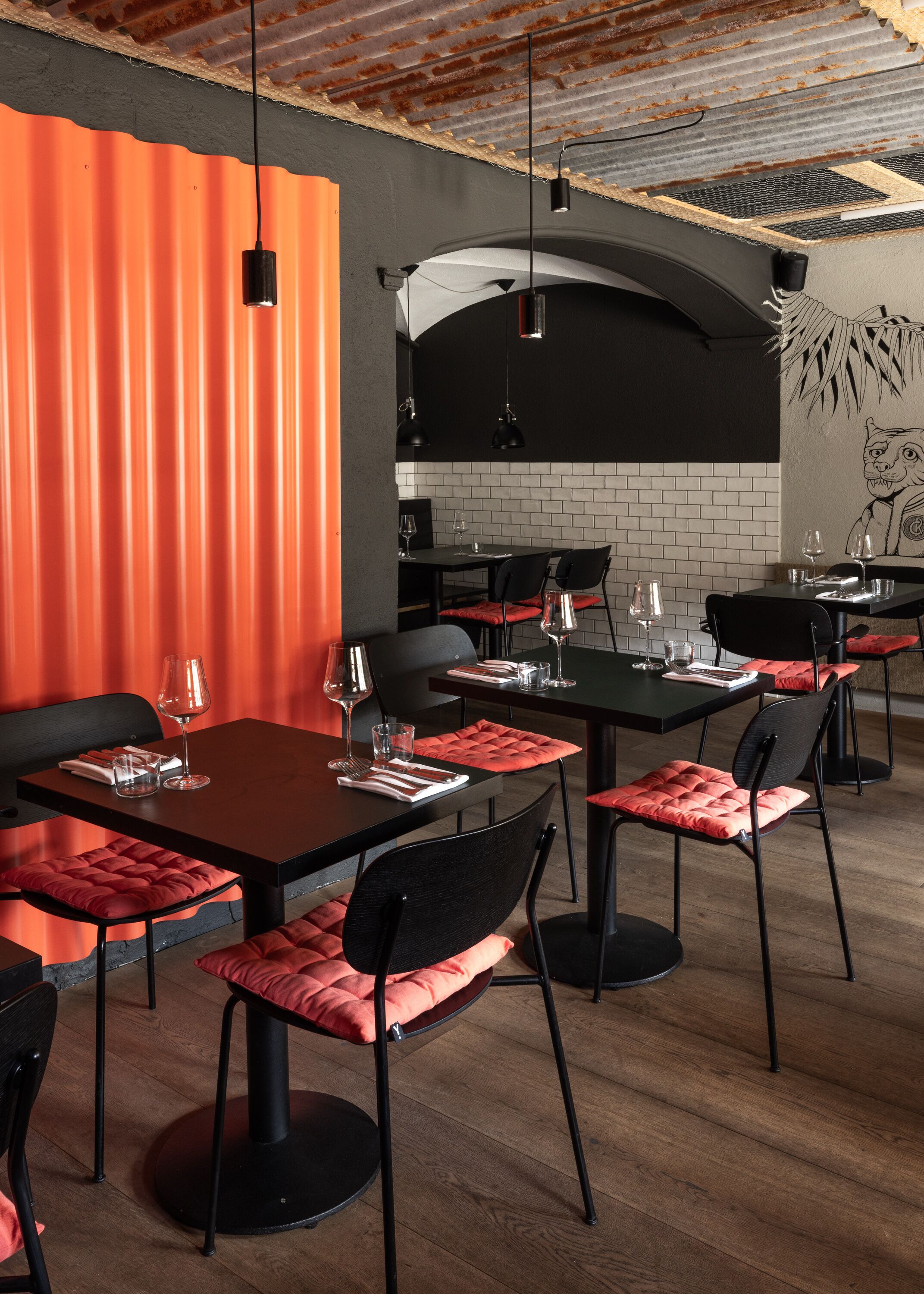 A restaurant interior with red and black decor, featuring tables and chairs, hanging lights, and a brick wall.