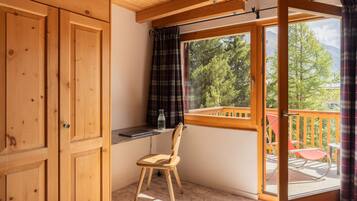 Un balcón de madera con vistas a árboles y montañas, una silla y una mesita.