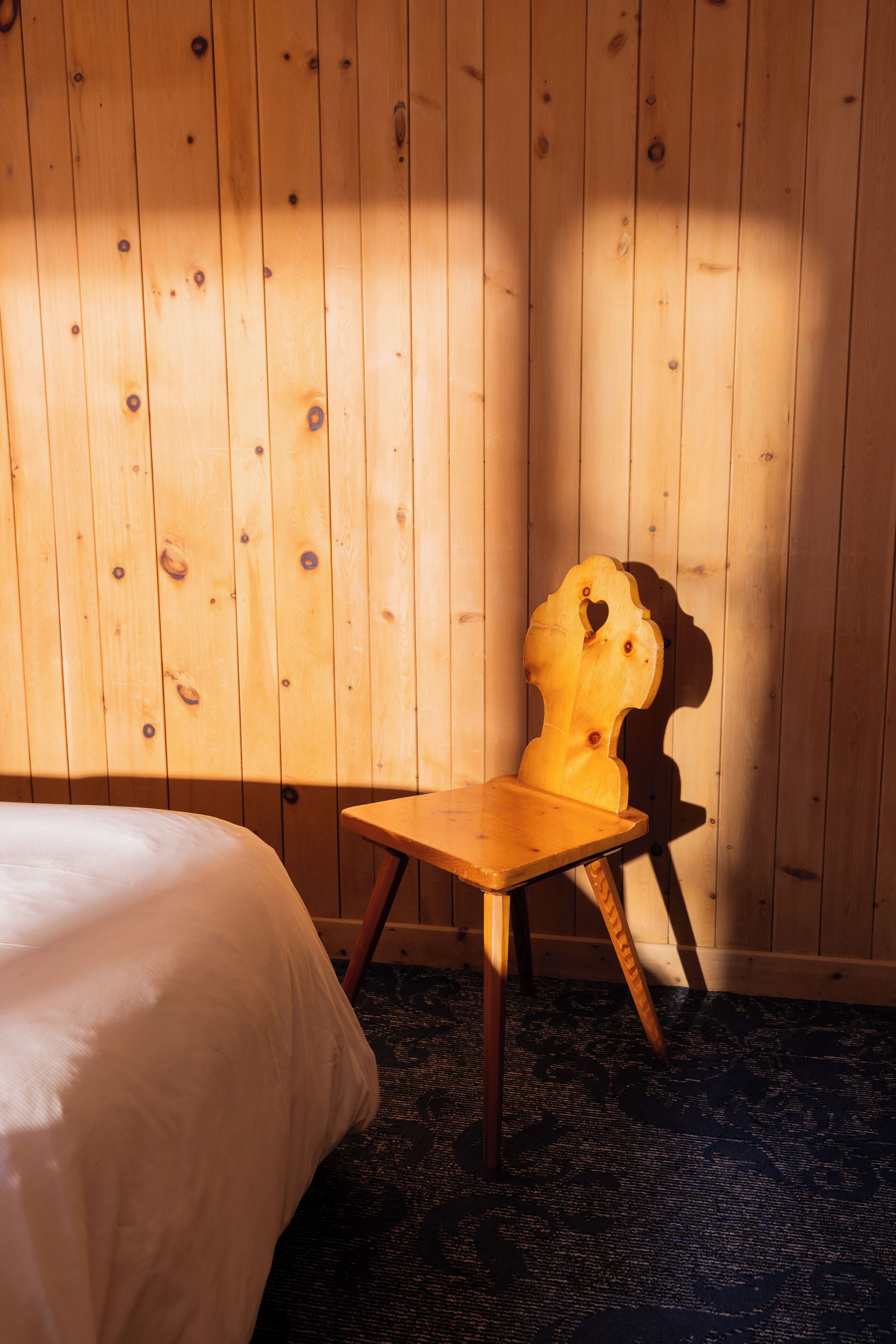 Uma cadeira de madeira com encosto em formato de coração em um quarto com paredes de madeira e carpete estampado.