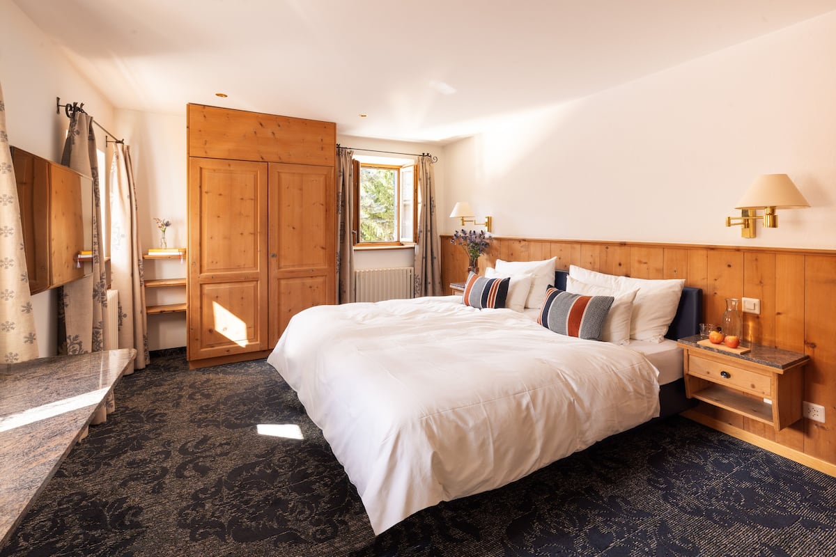 A bedroom with a large bed, wooden wardrobe, and a window with curtains.