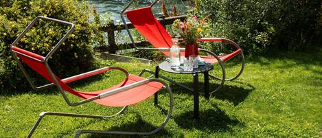 A red chair and table set on a grassy area with a river in the background.