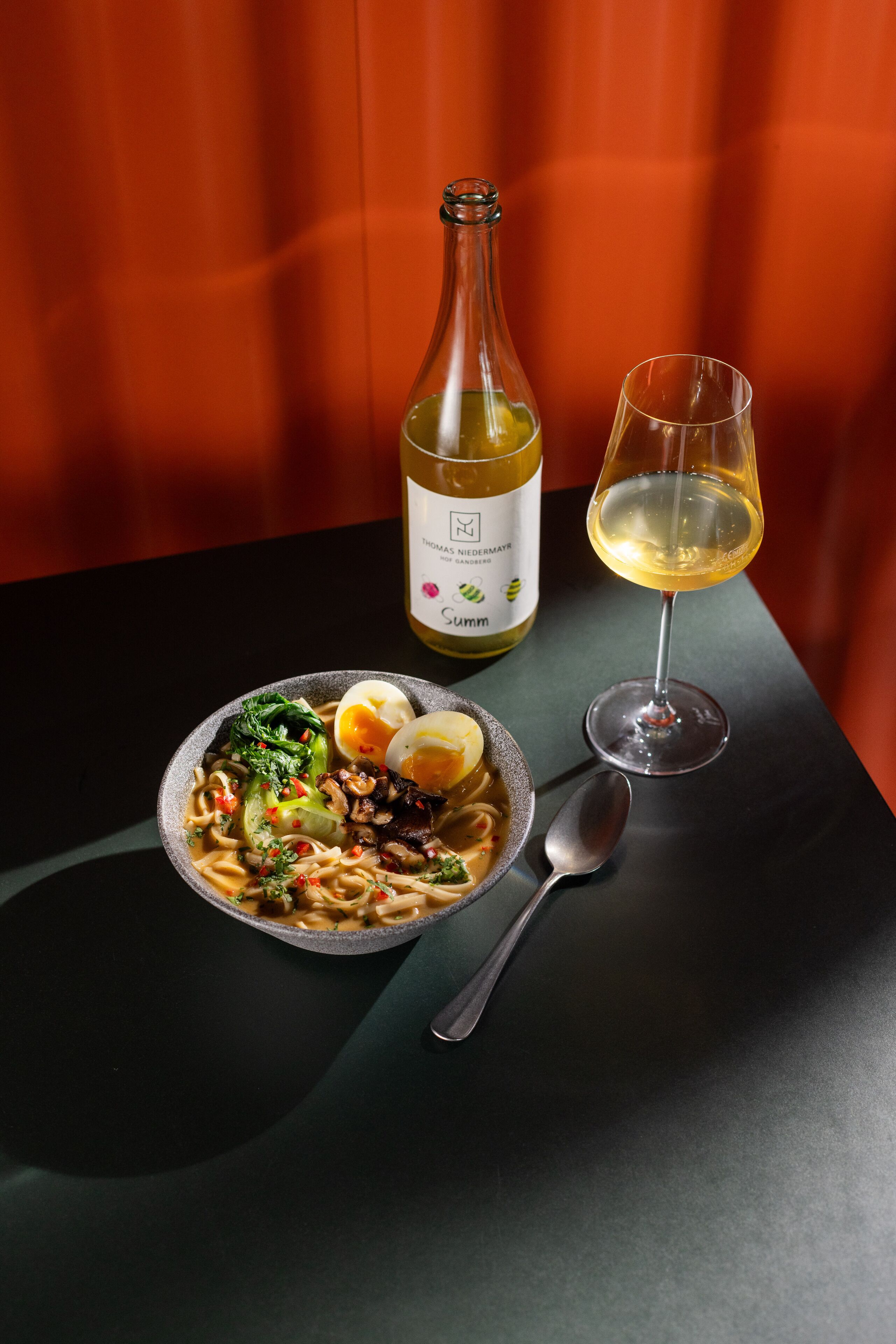 Une table avec un bol de nouilles, une bouteille de vin et un verre de vin.
