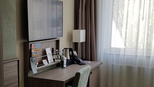 A hotel room with a desk, chair, television, and a window with curtains. - Best Western Plus Hotel Regence (Aachen)