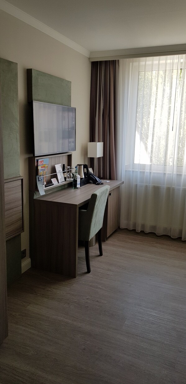 A hotel room with a desk, chair, television, and a window with curtains. - Best Western Plus Hotel Regence (Aachen)