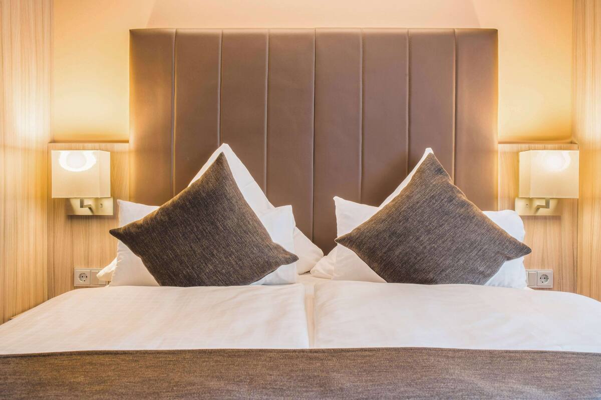 A hotel room with a large bed, two pillows, and bedside lamps.