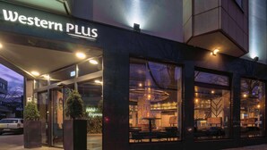A Western PLUS hotel exterior at dusk with large windows, outdoor seating, and a well-lit entrance.