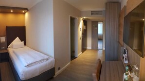 A hotel room with a bed, a desk, a TV, and a minibar. - Best Western Plus Hotel Regence (Aachen)
