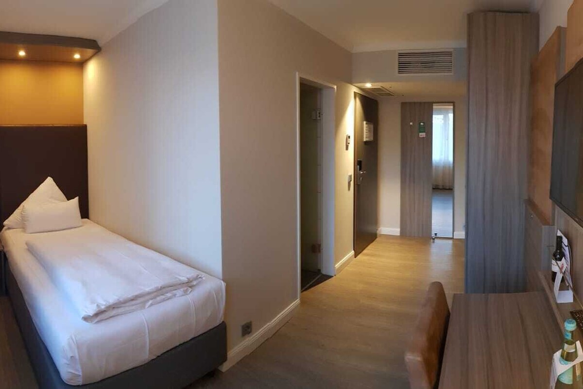 A hotel room with a bed, a desk, a TV, and a minibar.